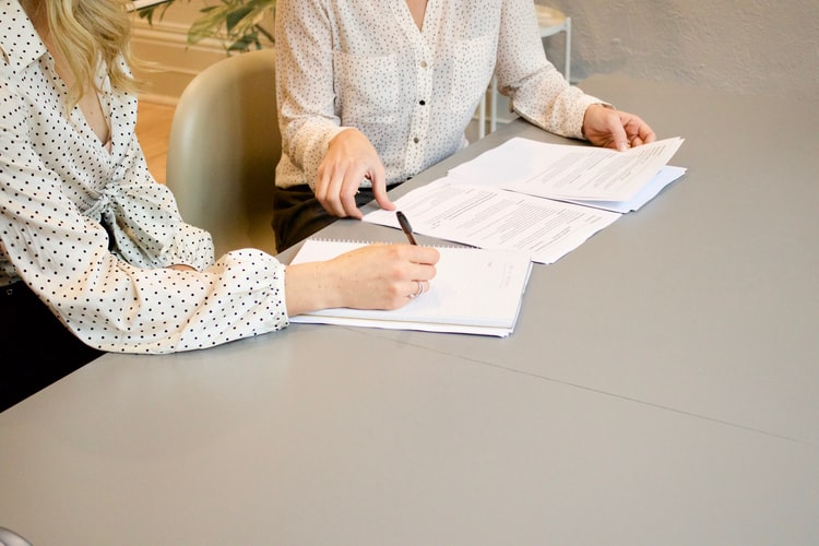 Two people sitting at a table looking at documentation and writing notes