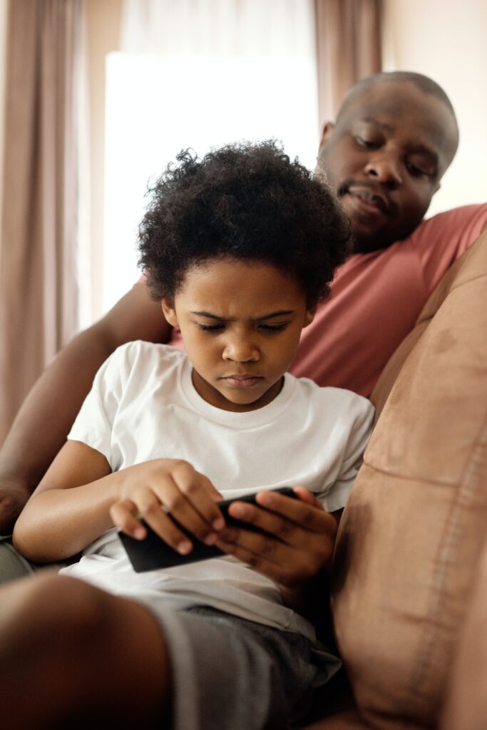 Man looking on at boy playing with smart phone
