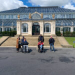 Five people from KCIL standing outside one of the other glass houses in Kew, two people are in wheelchairs