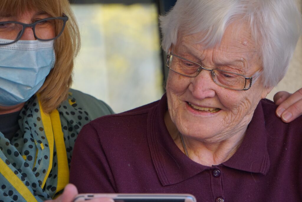 Woman in face mask helping older woman look at something on a phone