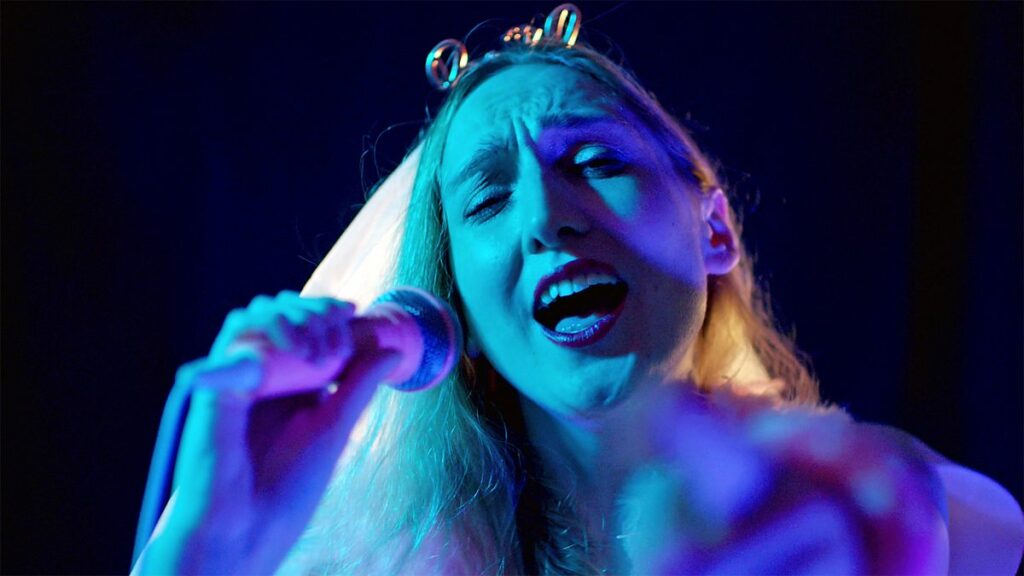 A young woman in a hen night outfit of a veil and tiara sings into a microphone
