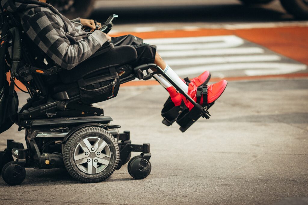 A photo showing a wheelchair user from the neck down, outside, next to a road