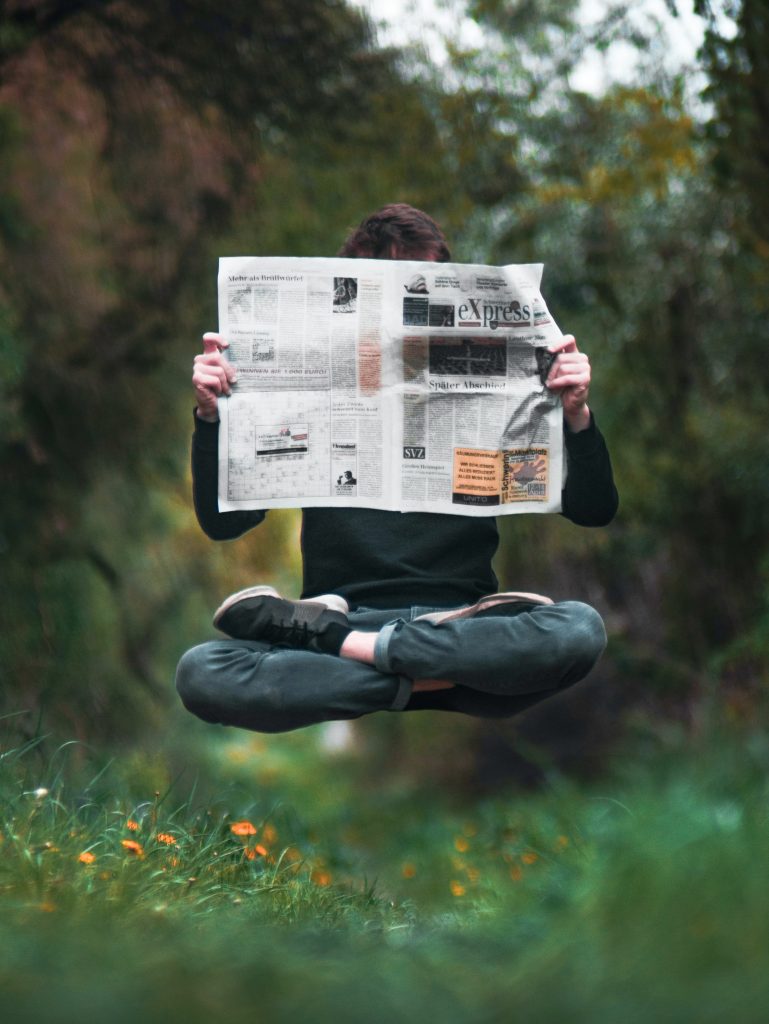 A person hovers above the ground, cross legged, whilst reading a newspaper