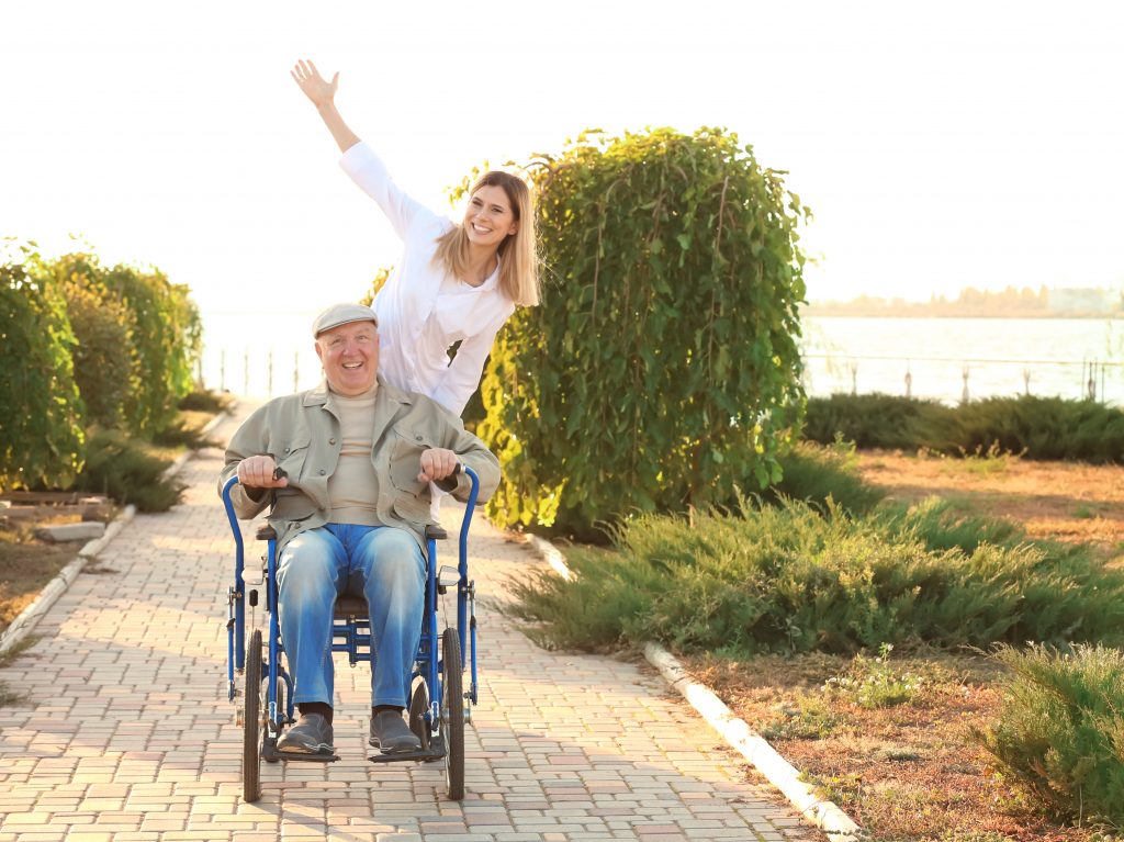 A cheerful woman pushes an older man along a path in a wheelchair