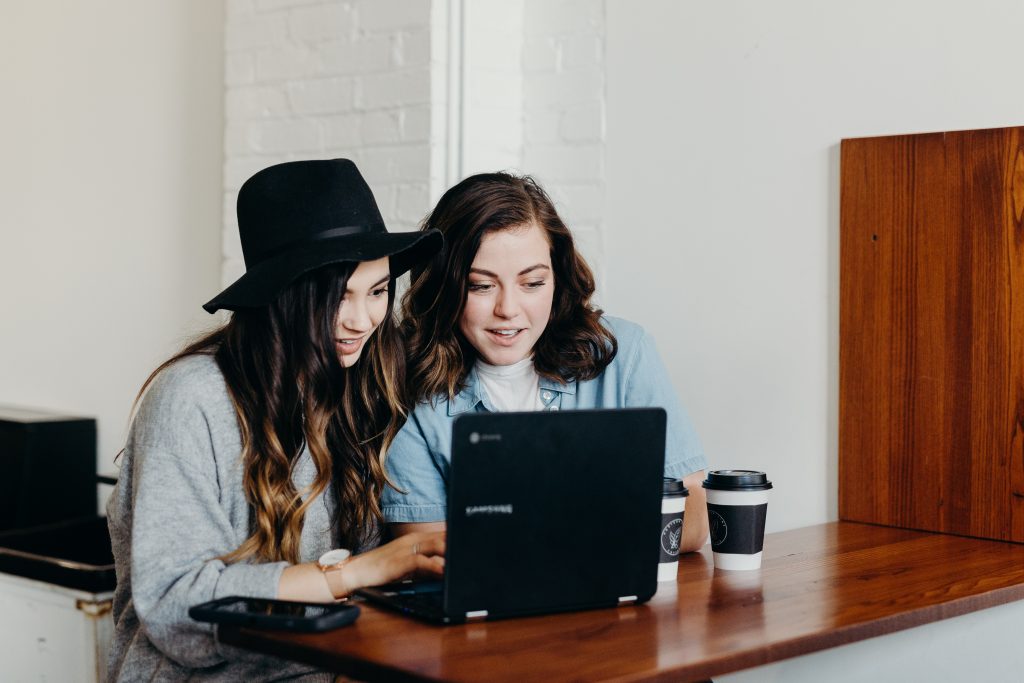 Two women sit in front of a laptop