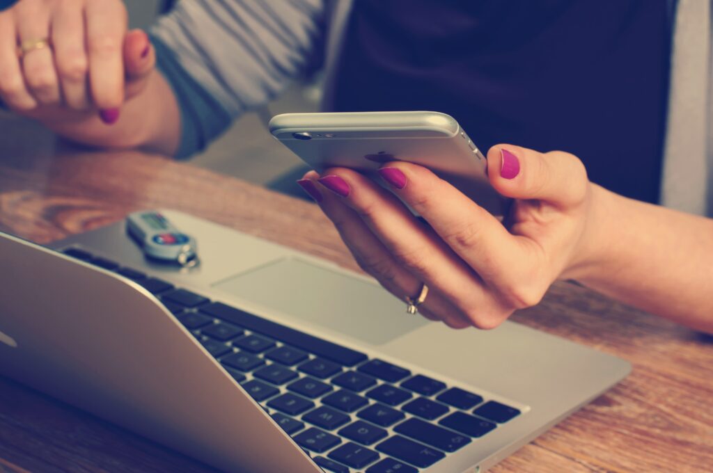 A woman in front of a laptop with phone in her hand