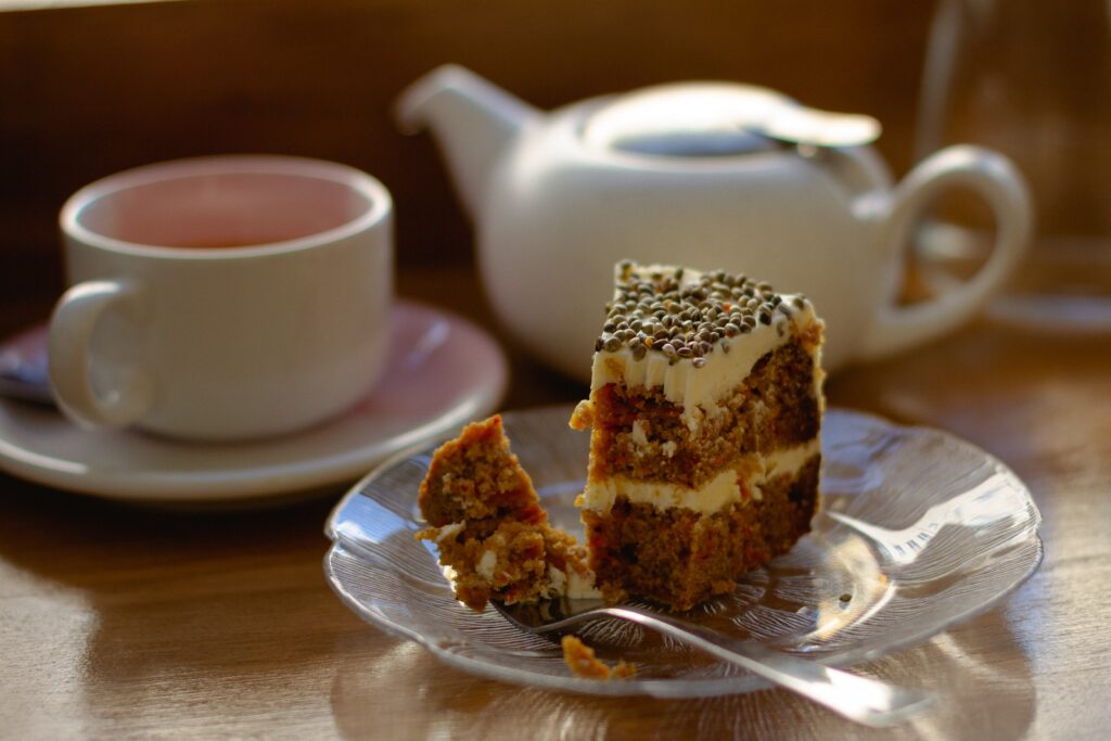 A cosy scene of a pot of tea, a cup and saucer and a delicious looking partially eaten slice of cake