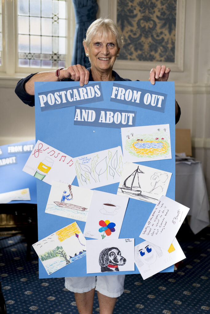 A volunteer from Conquest Art is holding up the finished poster with examples of everyone's work