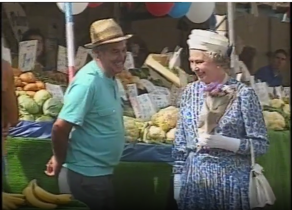 The Queen visiting Kingston Market in 1992 She is holding a bunch of flowers and is smiling. A stall holder next to her has a beaming smile.