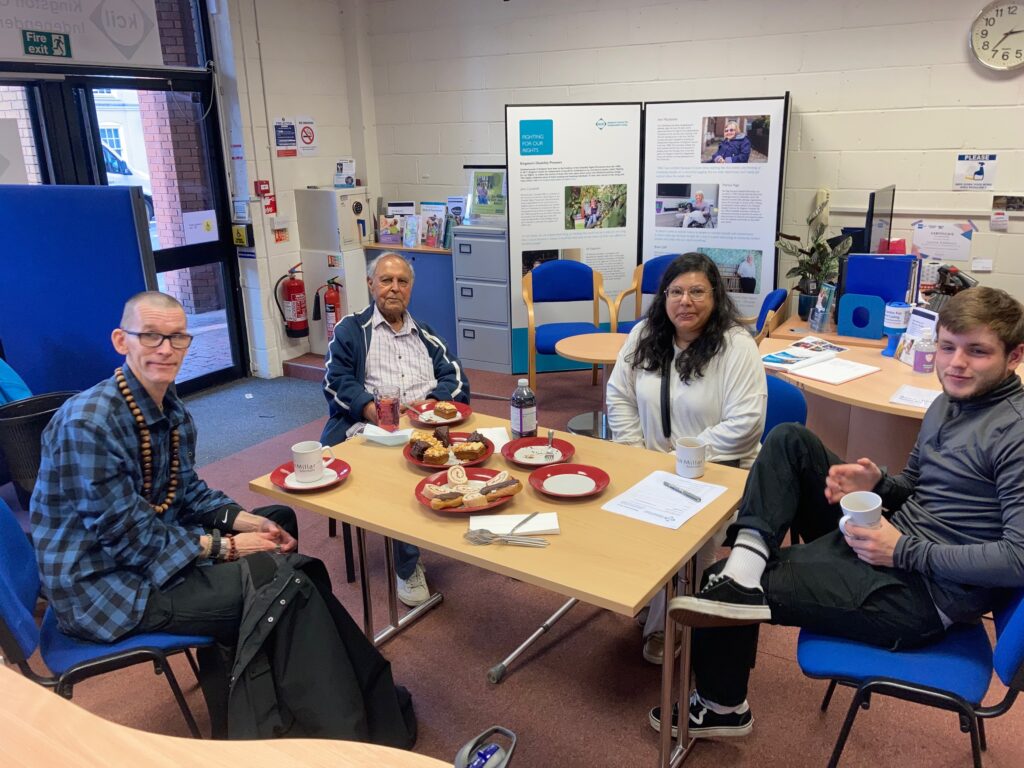 An image of four people sat around a table eating cake and drinking tea.