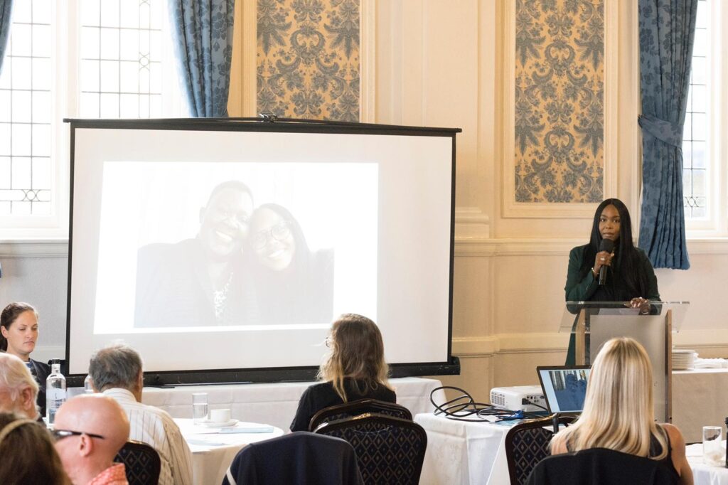 Meg speaking to the conference attendees. On the screen behind her is a photo of herself and her teacher