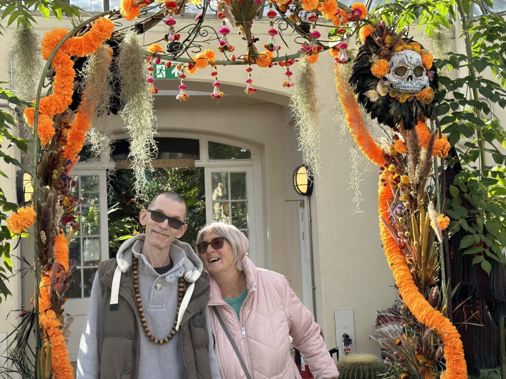 An image of a man and a woman stood under a Halloween themed flower arch.