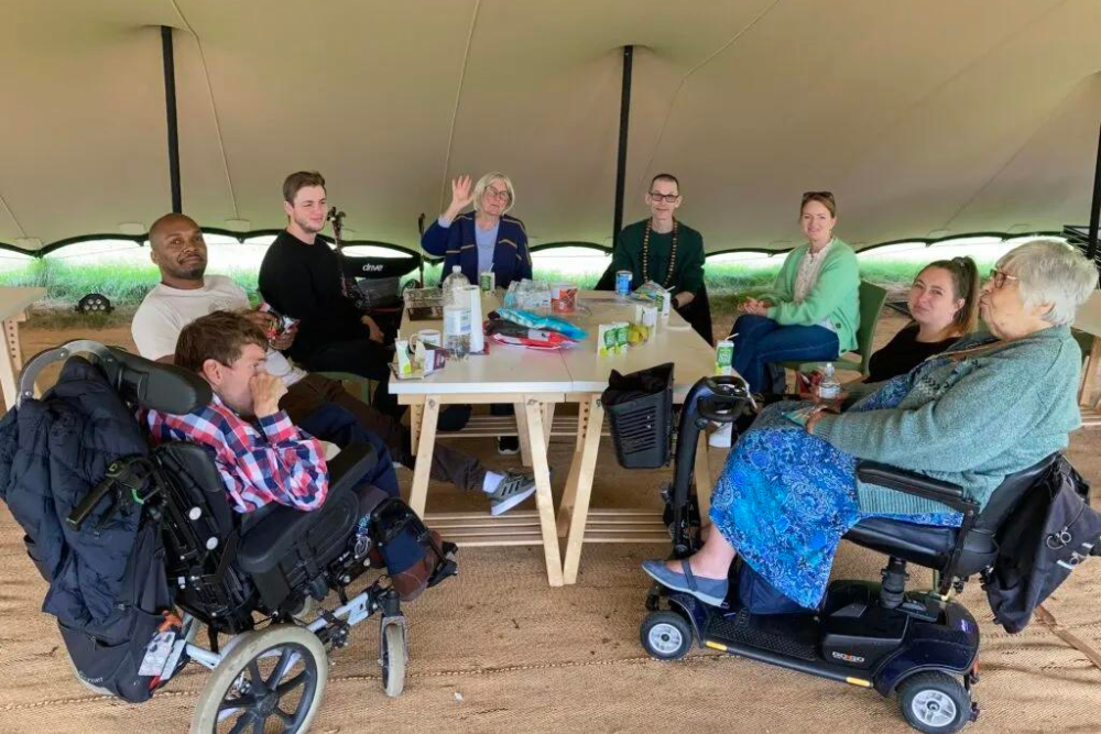 A group of people, some in wheelchairs, around an outside table underneath an awning
