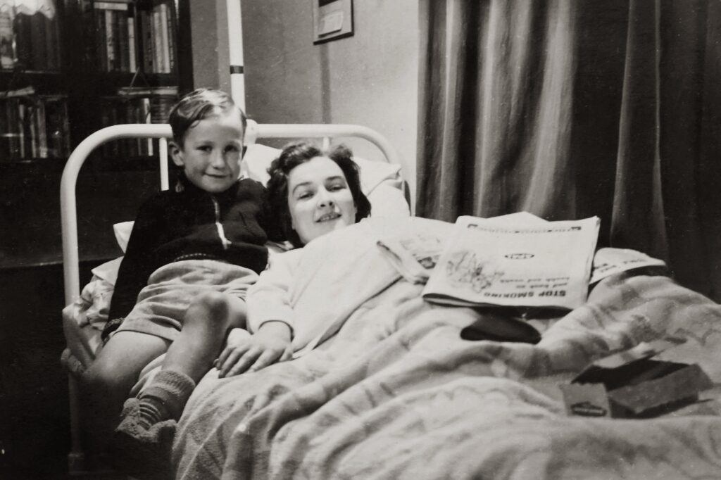 A black and white vintage photo, a woman is in a hospital bed, a young boy sits beside her