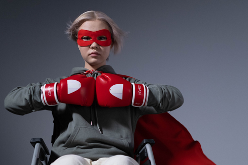 Superhero girl with red mask, boxing gloves and cape, in a wheelchair