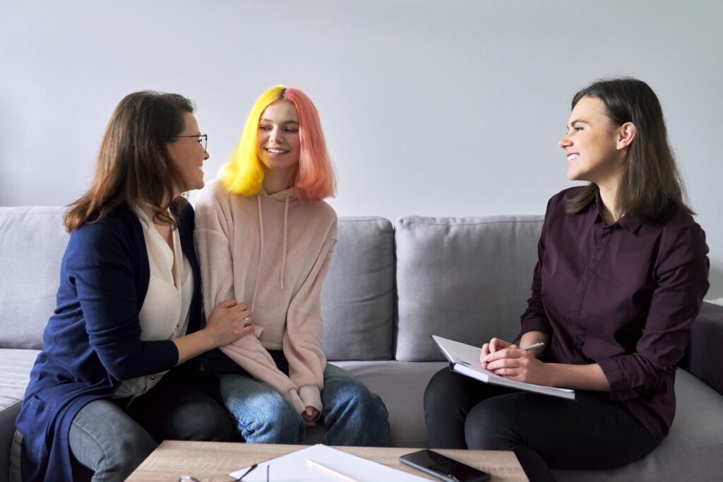 A mum and daughter sitting on a sofa, meeting with a person with a note pad