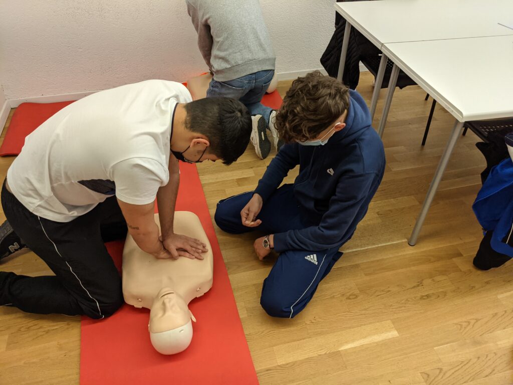 Two people kneeling on the floor practicing CPR on a dummy