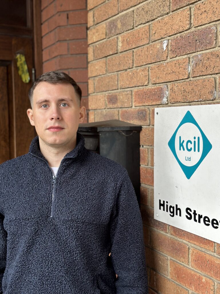 William stands next to the KCIL sign by the front entrance to the office