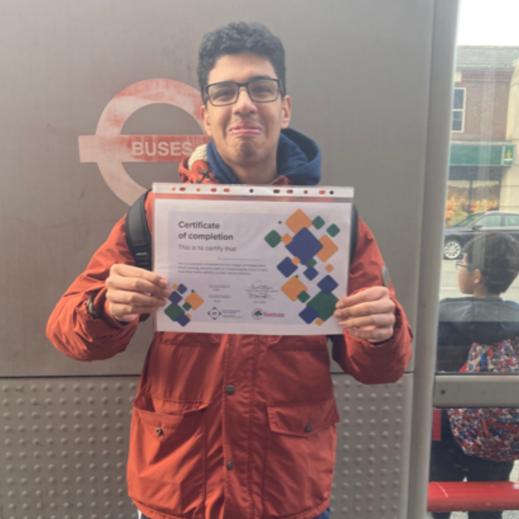 An ITT student holds up his certificate behind a bus stop