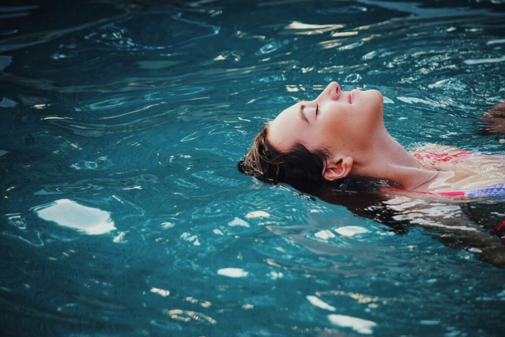A woman floats on her back in water, eyes closed