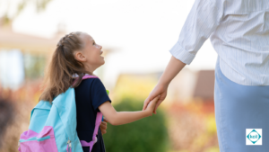 A young girl on the way to school holding a woman's hand