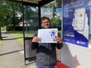 A young person holds his travel training certificate up to the camera while standing at a bus stop