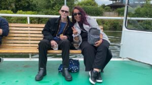 A KCIL service user and his PA sit on a bench, smiling at the camera, on the boat