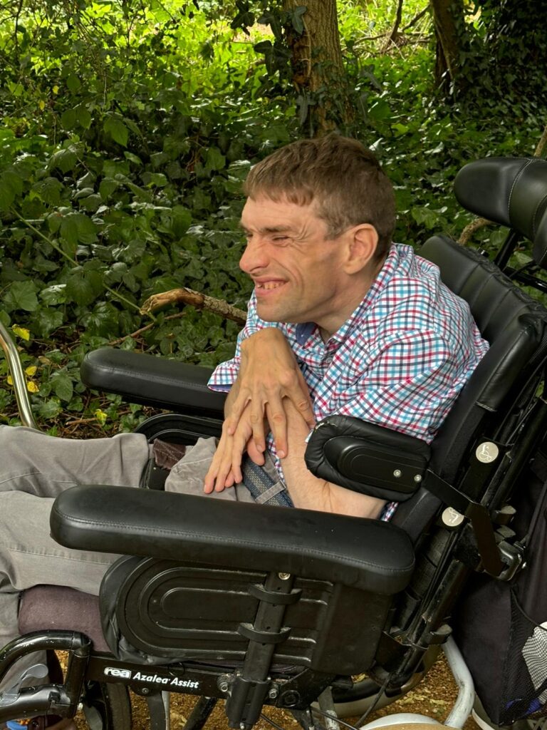 A KCIL service user at Edith Gardens, grinning in his wheelchair