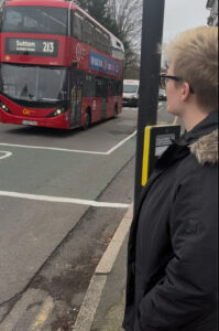 A young person stands by a pelican crossing as a Sutton bus goes by