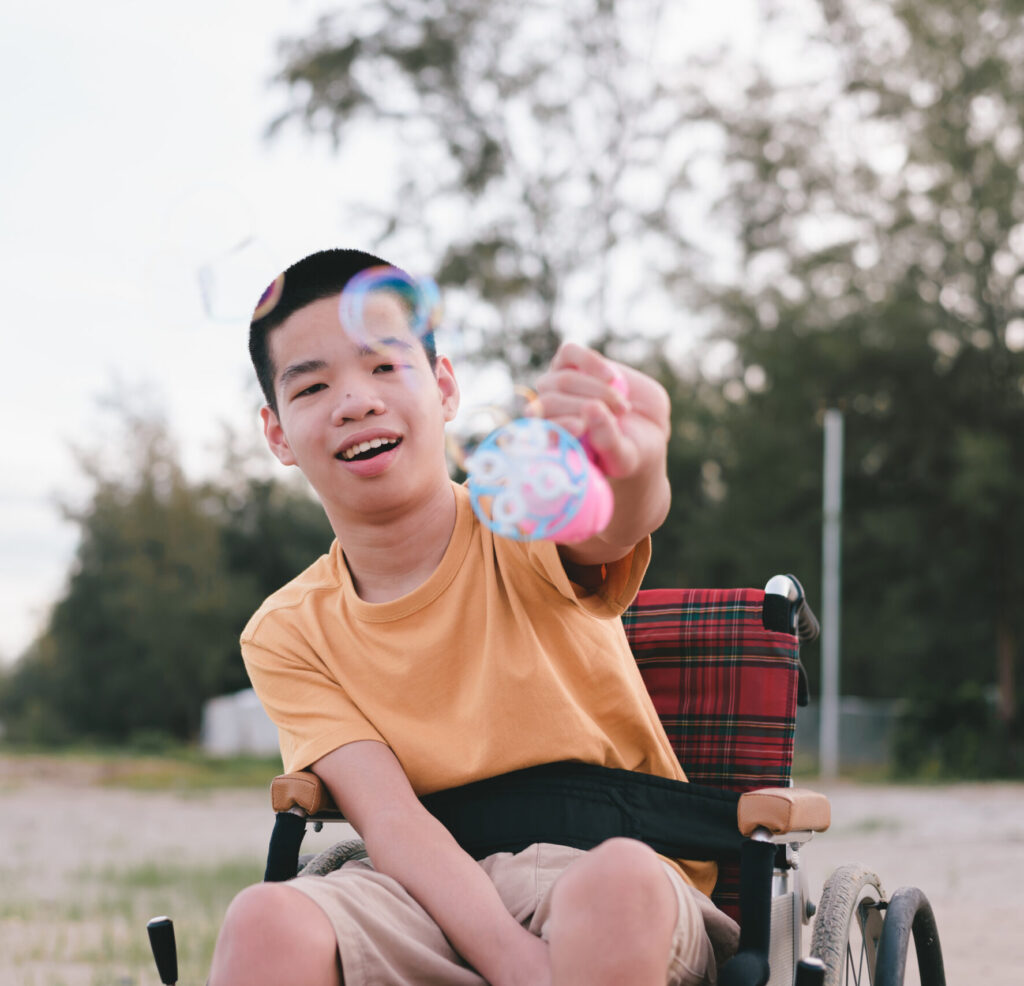 A young boy sitting in a wheelchair plays with bubbles