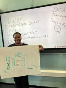 Natalina in front of a white board holding up one of the maps drawn by a student
