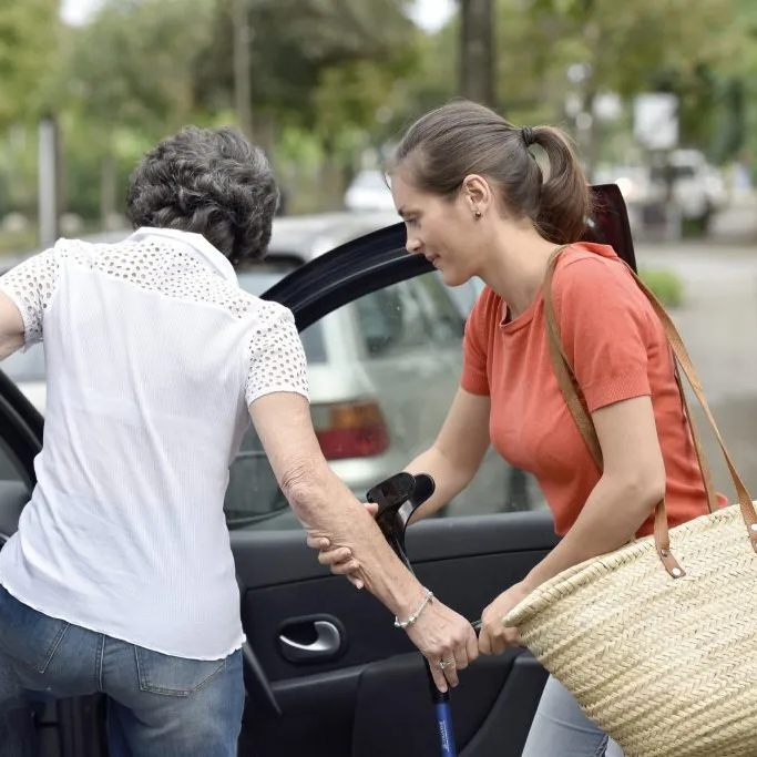 A young woman helps an older woman into a car