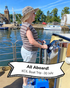 A KCIL trustee steering the boat, text reads All Aboard! KCIL Boat Trip 30 July
